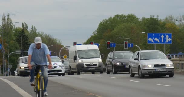 Dos hombres en las bicicletas diferentes coches pasan por el camino pavimentado Auto Road Marcando señales de tráfico y luces Encrucijada Paisaje urbano Nublado Día de Otoño Opole Polonia — Vídeo de stock