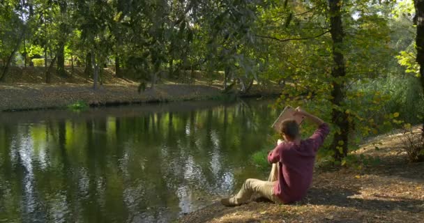 Man met rugzak komt naar rivier helling nam de laptop freelance programmeur ontwerper copywriter accountant zit op de grond begint te werken met laptop — Stockvideo