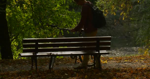 Muž v brýlích s batohu na kole se zastavil a sundal si batoh Posaďte se na lavičku, vraťte mu batoh na lavici. — Stock video