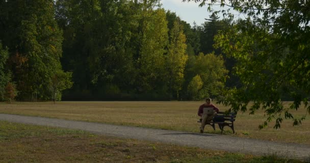 Man in Glasses is Sitting on the Bench Half Turned Freelance Programmer Designer Copywriter Accountant Working with Laptop Puts Laptop into Backpack — Stock Video