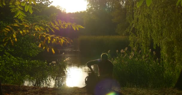 Silhouette de l'homme est assis sur la rive du lac avec ordinateur portable programmeur freelance concepteur rédacteur comptable mettre l'ordinateur portable dans sac à dos marche loin — Video