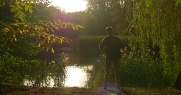 Man met rugzak silhouet komt op voet nam zijn rugzak uit zit op Lake Bank met laptop freelance programmeur ontwerper copywriter accountant — Stockvideo