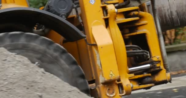 La excavadora amarilla está moviendo la excavadora de piernas del conductor Primer plano Seguimiento de la cámara izquierda sigue las piezas de la máquina de concreto Valla de seguridad de reparación de carreteras — Vídeos de Stock