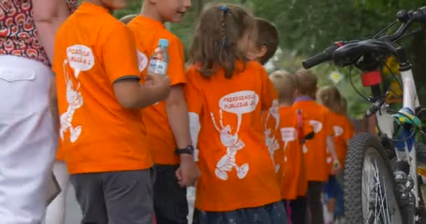 Педагоги ведуть групу дітей в помаранчевих футболках люди ходять по вулицях міста люди спиною велосипеда стоїть крупним планом дороги міста — стокове відео
