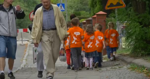 Группа детей в оранжевых футболках прогуливаются по улицам города, обращаясь к нужным педагогам — стоковое видео