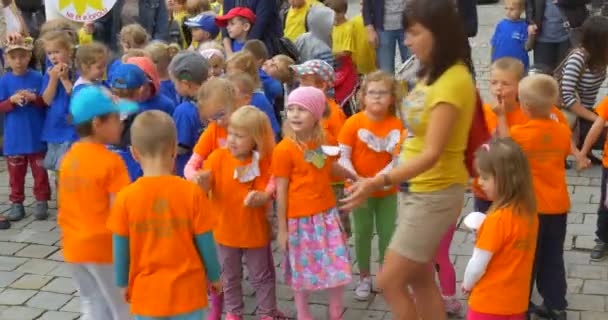 Группа детей в разноцветных футболках Дети прыгают Говорящие педагоги собираются Дети смотрят на педагога Люди на площади — стоковое видео