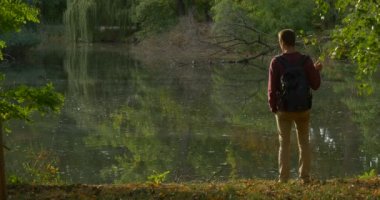 Sırt Çantası ile Man Orman Gölü Banck Geldi Su Düşmüş Kuru Treer Su Ağaçları 'Yansıması Rippling Su Ağaçları 'At Overgrown Bankalar Da Turist Walks Away