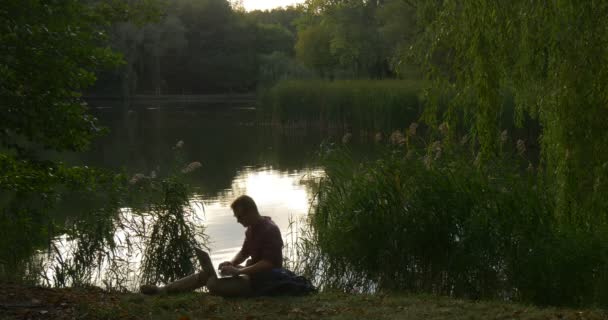 Uomo in bicchieri si siede al lago River Holding il computer portatile che lavora con il programmatore freelancer del computer portatile Copywriter Designer contabile stand up alberi verdi — Video Stock