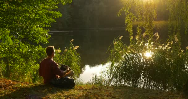 Людина в окулярах працює з ноутбуком сидячи в озері з його обличчям до сонця Фрілансер Програміст Копірайтер Дизайнер Бухгалтер Покласти ноутбук геть — стокове відео