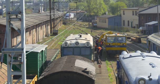 Gelbe Lokomotive mit ein paar beladenen entfernten Arbeitern Männer in orangefarbener Arbeitskleidung entladen die metallenen Detailwaggons auf den Dächern der Bahnhöfe und sonnigem Tag — Stockvideo