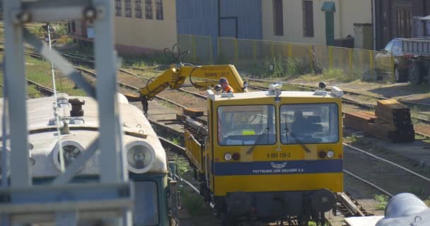 Gelbe Lokomotive entlädt die Bahnschwellen Lokführer Männer in orangefarbener Arbeitskleidung entladen die Metallteile der Waggons Dächer des Bahnhofs — Stockvideo