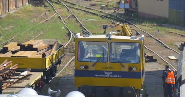 Gelbe Lokomotive bewegt sich auf die Kamera zu und stoppt Kran auf Lokomotivführer nähert sich dem Kranführer spricht mit Arbeitern sonnigen Tag — Stockvideo