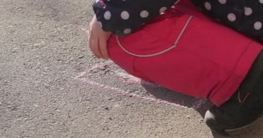 Kızın ellerini çocuk üzerinde boyama pembe parça tebeşir çocuk tarafından Walkside dönüm pembe pantolon ceket lekeli çizme resmi asfalt üzerinde olduğunu
