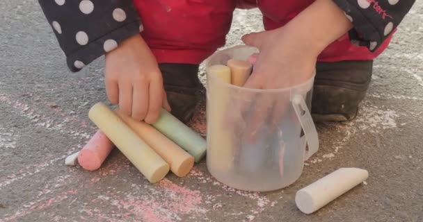 Meisje handjes zetten kleurrijke krijtjes aan het kleine Plastic emmer meisje in jas in Polka Dots laarzen afbeelding op asfalt Winter Outdoors — Stockvideo