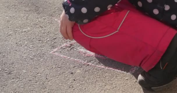 Manos del niño de la muchacha está pintando en la caminata por el pedazo rosado de tiza El niño está dando vuelta la chaqueta rosada de los pantalones en botas de lunares Foto en el asfalto — Vídeos de Stock