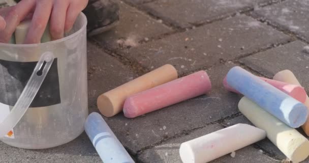 Kleine Mädchenhände aus nächster Nähe, die ihre Kreidestücke in Plastikeimern sammeln Mädchen mit Hut und rosa Hose Mädchen sitzt auf dem Asphalt — Stockvideo