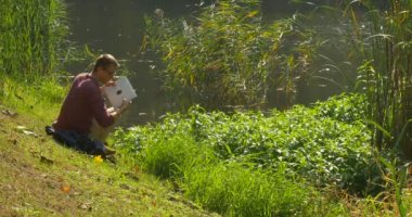 Laptop ile Man Lake Bank Freelancer Programcı Corywriter Tasarımcı Muhasebeci Üzerinde Oturuyor Sırt Çantası Içine Laptop koyun Çalışıyor Away Walks