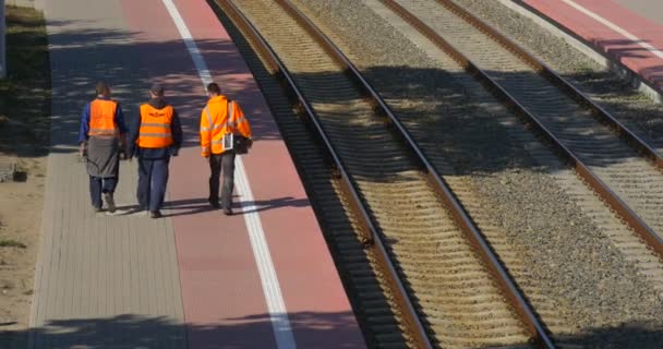 Três trabalhadores homens em roupas de trabalho laranja estão caminhando ao longo da ferrovia vazia Men 's Backs Estação Ferroviária Ferroviária Junção Ferroviária semáforos — Vídeo de Stock