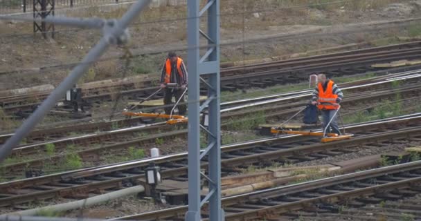 Dva dělníci v oranžovém pracovním oblečení chodí rychle po železnici po trati se speciálním nástrojem na sledování kol vlevo — Stock video