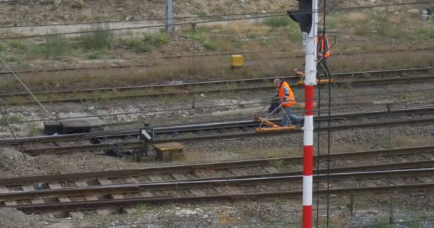Due operai in abiti da lavoro arancioni camminano veloci lungo la ferrovia controllando la ferrovia con uno strumento speciale sul semaforo delle ruote Mid Shot — Video Stock