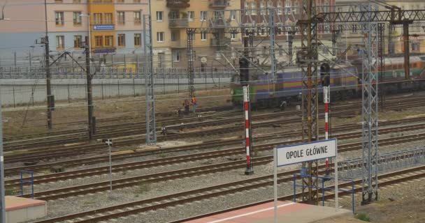 Tren de mercancías llega a los vagones de locomotoras Edificios Casas residenciales detrás de la valla Torres de alambre Inscripción en la estación ferroviaria polaca Plataforma ferroviaria — Vídeo de stock