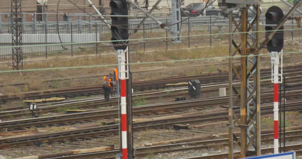 Dwóch pracowników w Orange Odzież robocza sprawdza Railroad Wire Towers przewody Sity Street na tle Walking Man Distantly samochody zachmurzone — Wideo stockowe