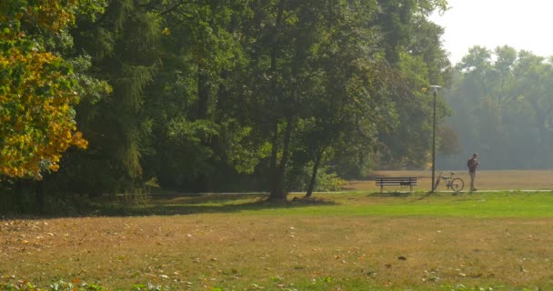 Man heeft stond op uit de Bank wandelen lezing de boek permanent draaien lopen weer breed Shot fiets is permanent op straat Lamp Reader in Park — Stockvideo