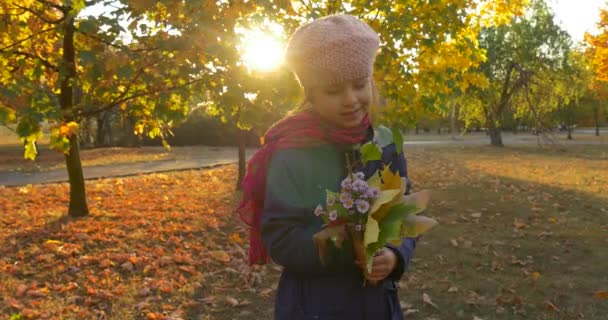 Petite fille avec belle fille tresse en béret et veste se tient debout et regarde son bouquet composé de feuilles d'érable jaunes et de fleurs qui parlent en souriant — Video