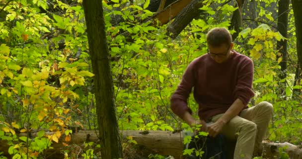 Man in Glasses is Sitting on a Fallen Tree Trunk Freelancer Programmer Copywriter Designer Accountant is Working with Laptop Takes the Book Reading — Stock Video