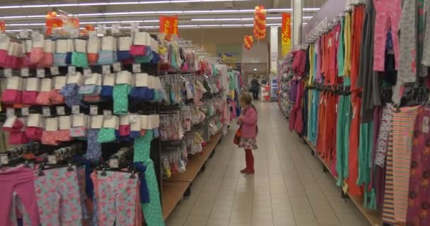 Девушка в отделе детской одежды смотрит на ценники товаров — стоковое видео