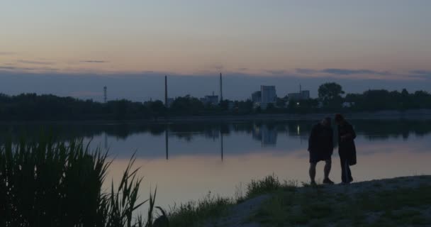 Siluety muže a ženy jsou chůze se psem u rybníka, řeky banky, modré večerní obloze, hladké vodě — Stock video