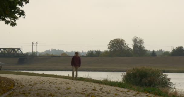 남자와 배낭은 강 공원 골목 남자 고 카메라 통해 강 흐린도 교량에 나뭇잎 떨어진 쪽으로 멀리 실행에 서 — 비디오