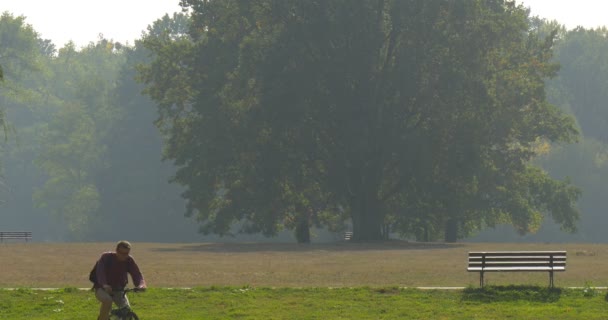 バックパックを持つ男は、路地生い茂った緑公園晴れた日秋秋の行楽で乗馬、自転車、カメラに向かって草原空ベンチ — ストック動画