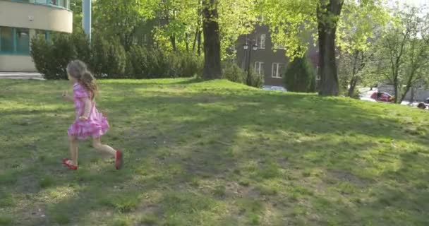 De Camera loopt voor babymeisje in een roze jurk in rode schoenen op groene Bleed — Stockvideo