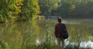 Sırt Çantası ile Man Lake Bank Kulaklıklar geliyor Sırt Çantası Man Bir Süre Adam Gözlük Walks Walks SAnd For Stood vardır Sarı Yapraklar Yeşil Reed Sunny