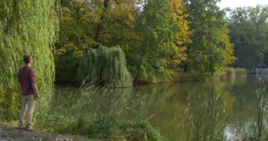 Adam gözlük Gölü banka geliyor ve yere adam oturur doğa ağaçlar ve yeşil Reed çevresinde yaprakları ağaçların üzerinde sarı çoğu gözlem