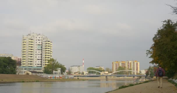 Az ember a hátizsák a gyaloglás Away by Asphalted Road in Park Alley leáll Turns visszatekintve Tourist Cityscape multi-Storeyed házak és a híd ősz — Stock videók