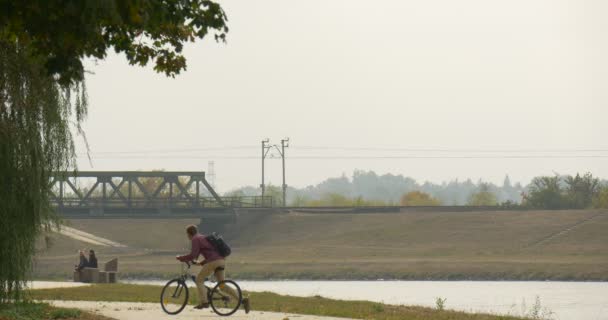 Homme à lunettes avec sac à dos a obtenu sur le vélo équitation le vélo loin se déplacer par allée asphaltée Les gens sont assis sur le banc sec feuilles tombantes — Video