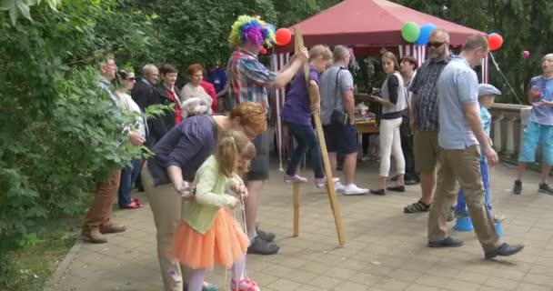 Palhaço em traje colorido ajuda as crianças a andar sobre palafitas sobre as crianças — Vídeo de Stock