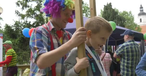 Clown in costume colorato aiuta a ragazzo a camminare su trampoli in vacanza all'aperto — Video Stock