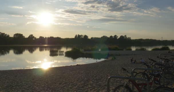 Stagno, Fiume, Spiaggia di sabbia del lago, Acqua increspata, Riflessione sugli alberi, Tramonto, Biciclette — Video Stock