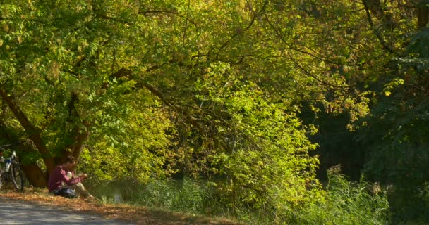 L'homme trouve dans le livre le bon endroit et commence à le lire L'homme en chemise marron et pantalon beige se trouve sous l'arbre vert écartant sur la colline près du lac 