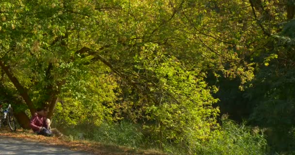 Homme met livre dans son sac à dos et prend ordinateur portable, il travaille sur ordinateur portable pigiste rédacteur concepteur comptable programmeur homme assis sous l'arbre de propagation 