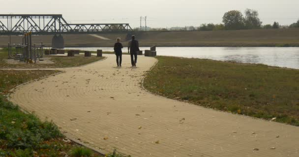 Hombre y mujer caminan por el camino pavimentado con losas de pavimentación caminan cerca del terreno deportivo en el parque Nublado Opole Polonia — Vídeos de Stock