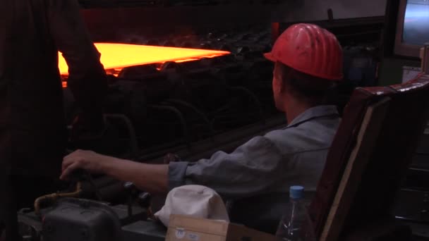 Twee werknemers in veiligheidshelmen bij de machine, het rollen van metaal, warmwalsen, rode hete metalen platen zijn aangekomen — Stockvideo