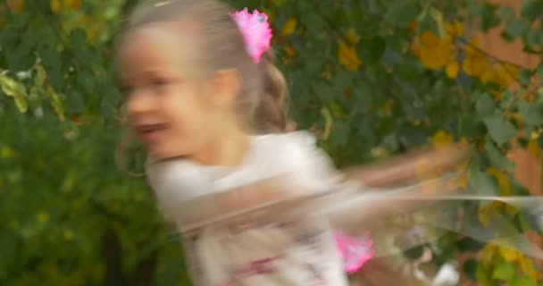 Malá blonďatá dívka s copem kýval růžový luky dívka v bílém tričku s její bílá taška Girl hraje v parku zelené a žluté listy na podzim — Stock video