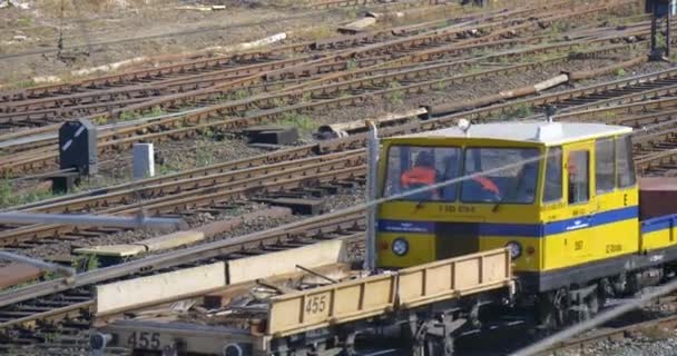 Arbeiter in orangefarbener Arbeitskleidung sitzen im Führerstand einer gelben Lokomotive, die die Lademaschine durch den Eisenbahnknotenpunkt transportiert