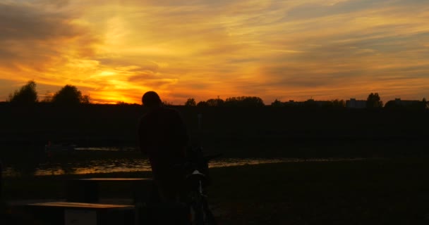 Man by Bicycle Comes to The Bench And Table at River Working with Laptop Freelance Programmer Designer Freelance Copywriter Accountant Bright Sunset — Stock Video