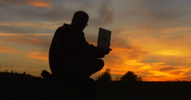 Uomo Silhouette L'uomo è seduto a terra sulla riva del campo di lavoro con il computer portatile freelance progettista freelance Copywriter ragioniere — Video Stock