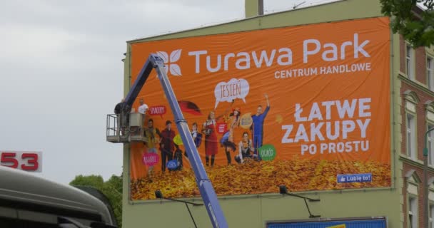 Dwóch mężczyzn pracowników w wieży Truck instalujesz pomarańczowy reklama Banner na metalowej ramie do okna czerwone bloki budowlane budynku — Wideo stockowe